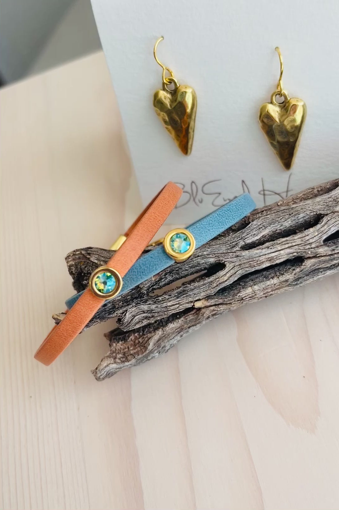 Video of Mini Ginger Bracelet and blue bracelet with gold heart shaped pendant  and driftwood in background on table
