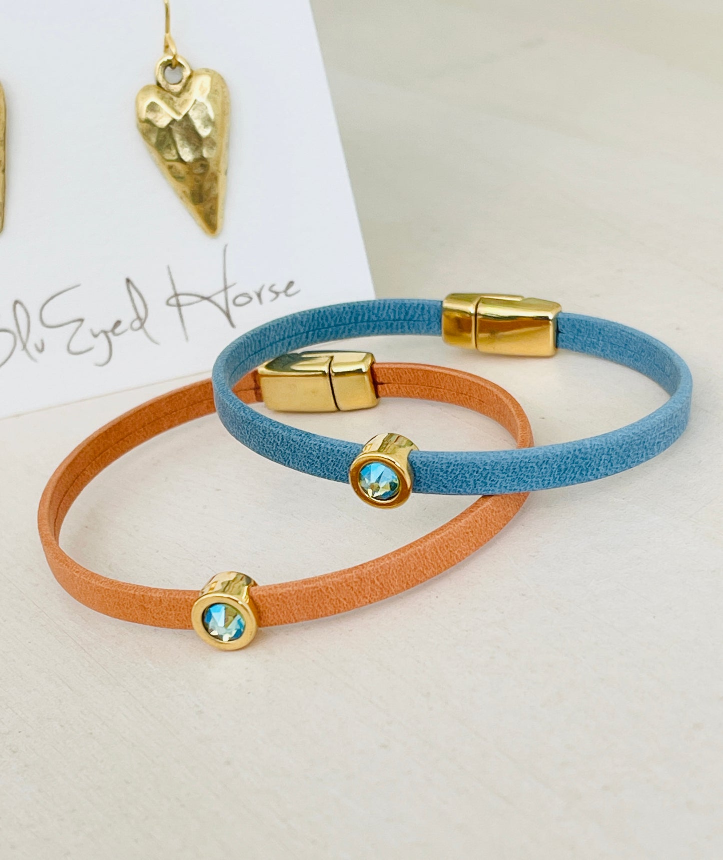 Mini Ginger Bracelet and blue bracelet with gold heart shaped pendant in background on table