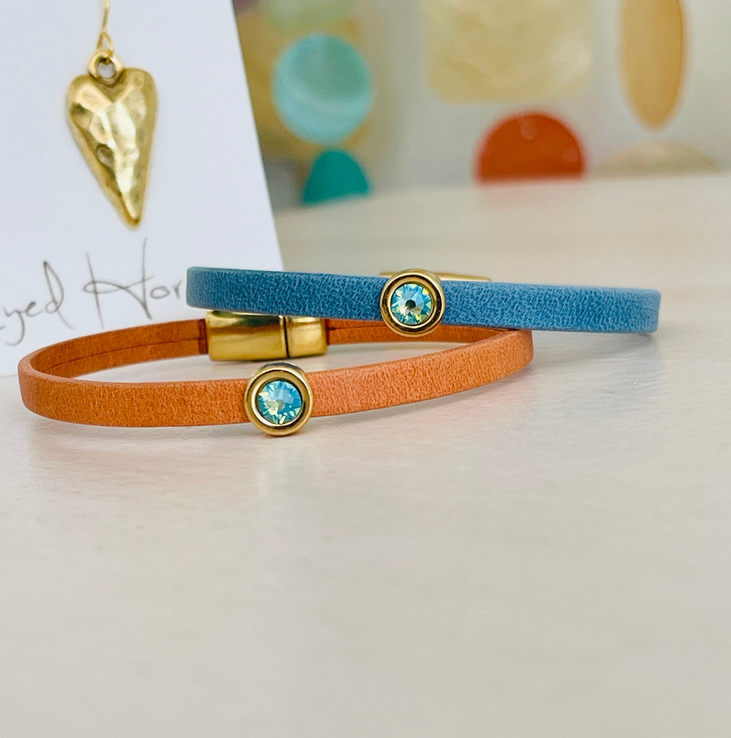 Mini Ginger Bracelet and blue bracelet with gold heart shaped pendant in background on table