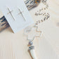 Carmen Necklace with cross earrings displayed on top of driftwood