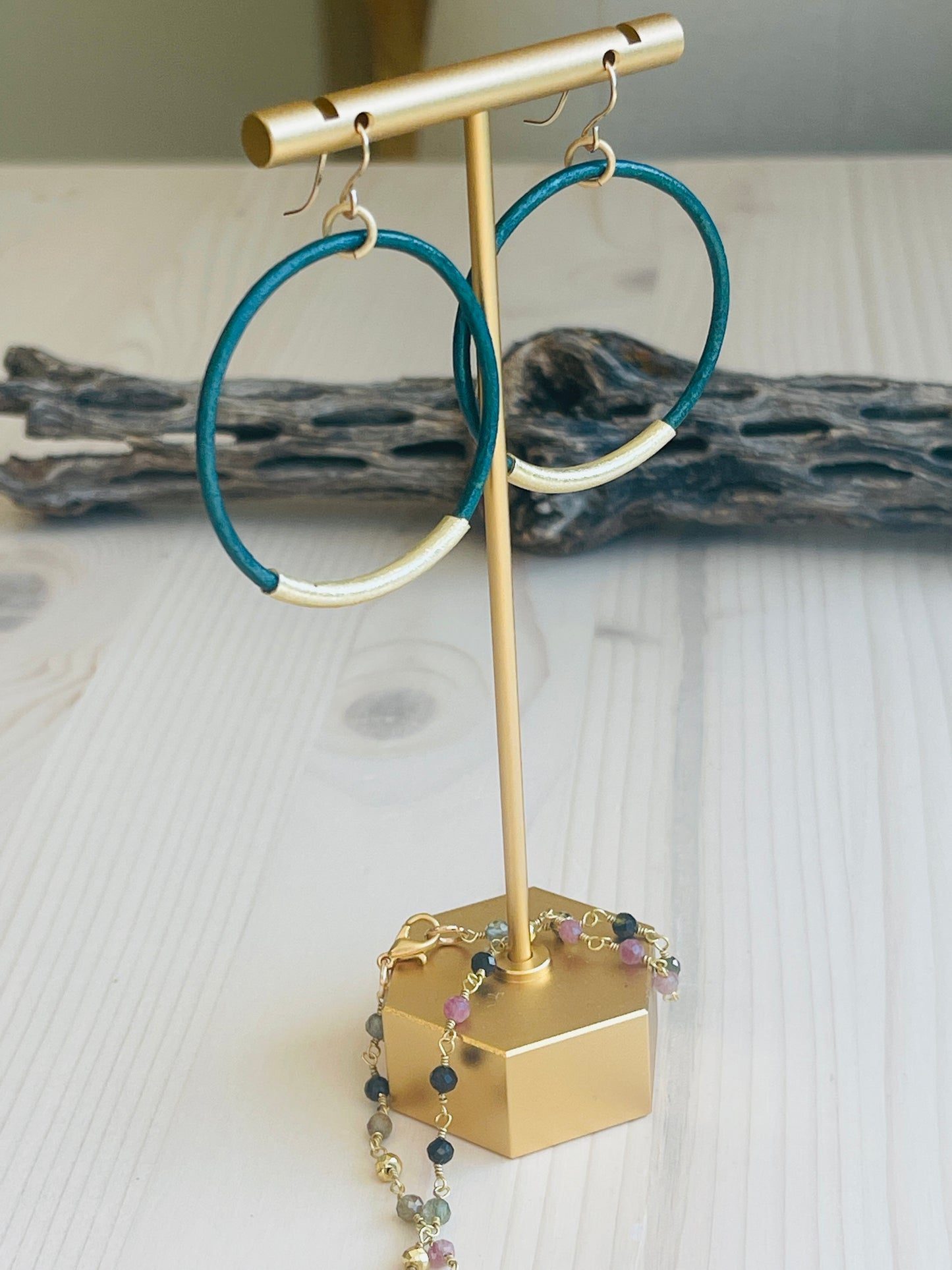 Teal Leather Hoops displayed on t-shaped stand with dirftwood in background