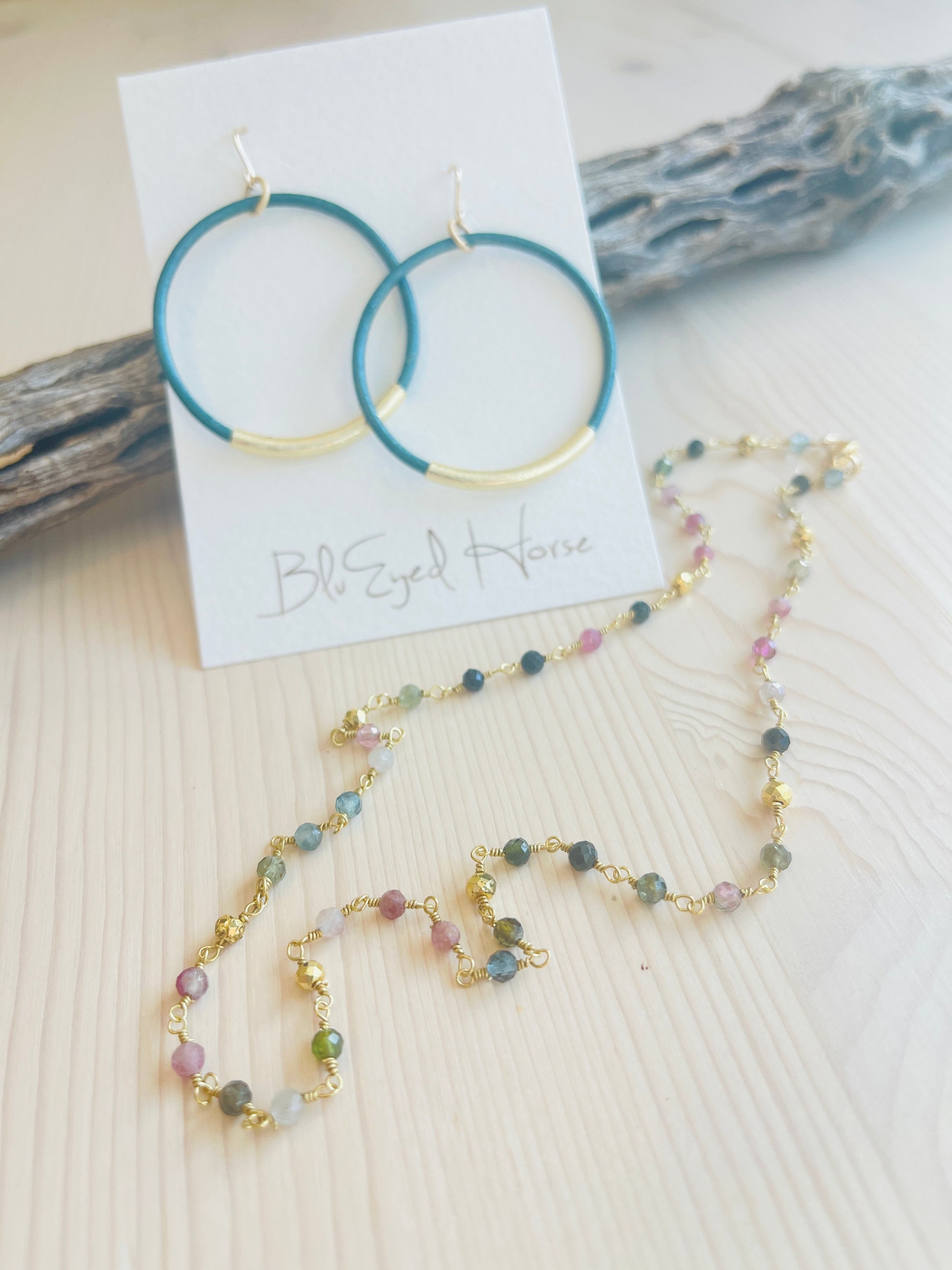 Tourmaline Choker with blue hoop earrings in the background displayed on driftwood